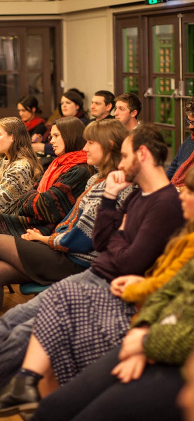 A crowd of seated people watching a poetry performance (performer outside of the frame)