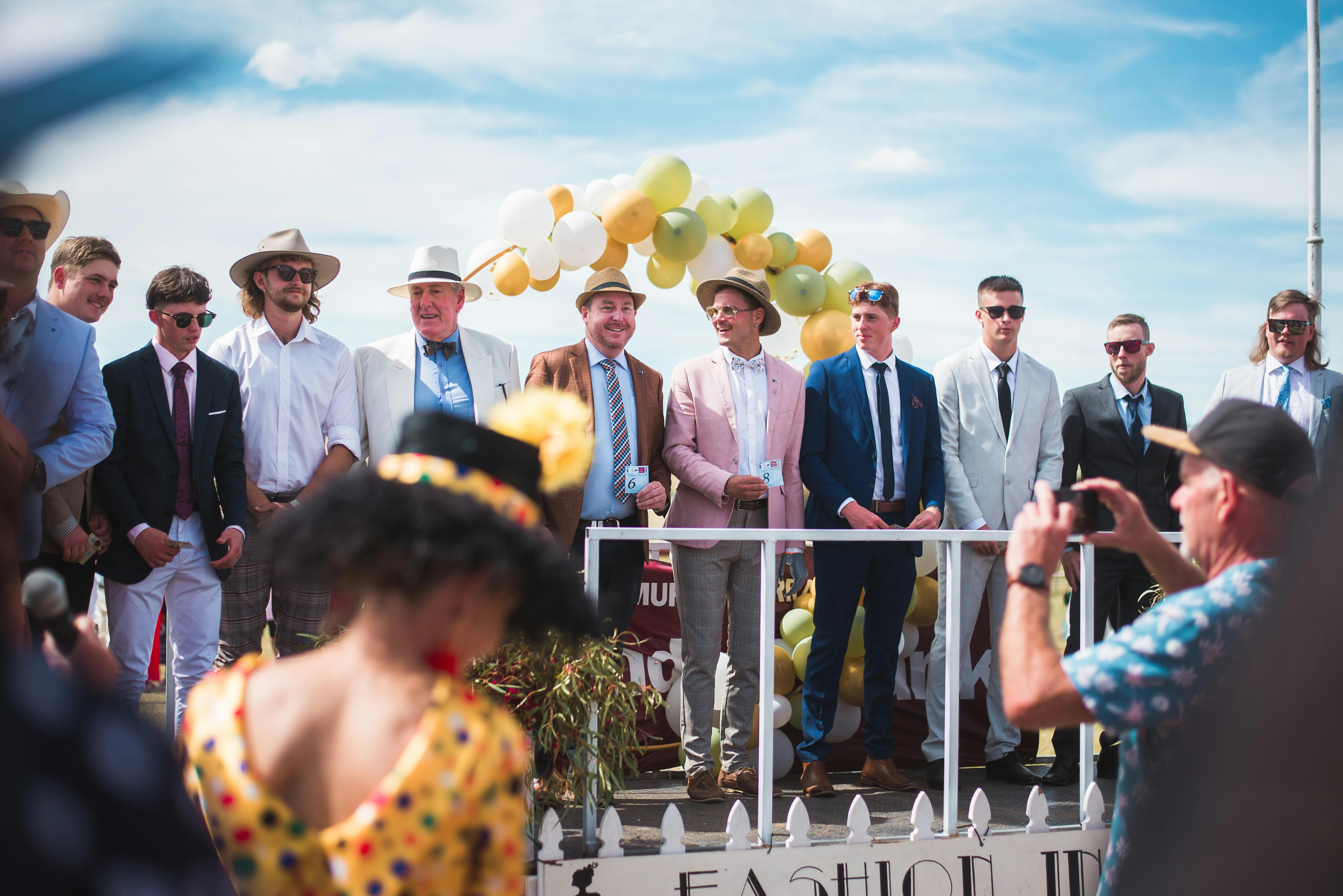 Ladies' Fashions on the Field - a yellow balloon arch behind them with a beautiful blue sky.