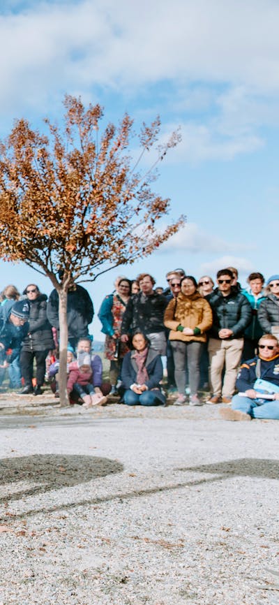 Person tending to a fire pit during a smoking ceremony, surrounded by a large crowd