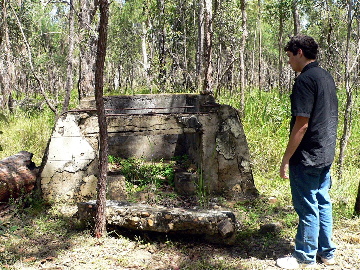 Adult male standing at remains of officers' mess fireplace.