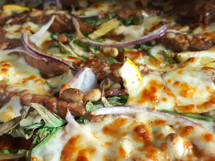 Close up of pizza with beef, onion, rocket, lemon slices and cheeseket