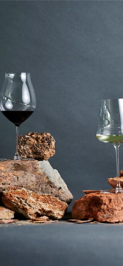 Glasses of wine are balanced on top of red clay soils in a studio shot.