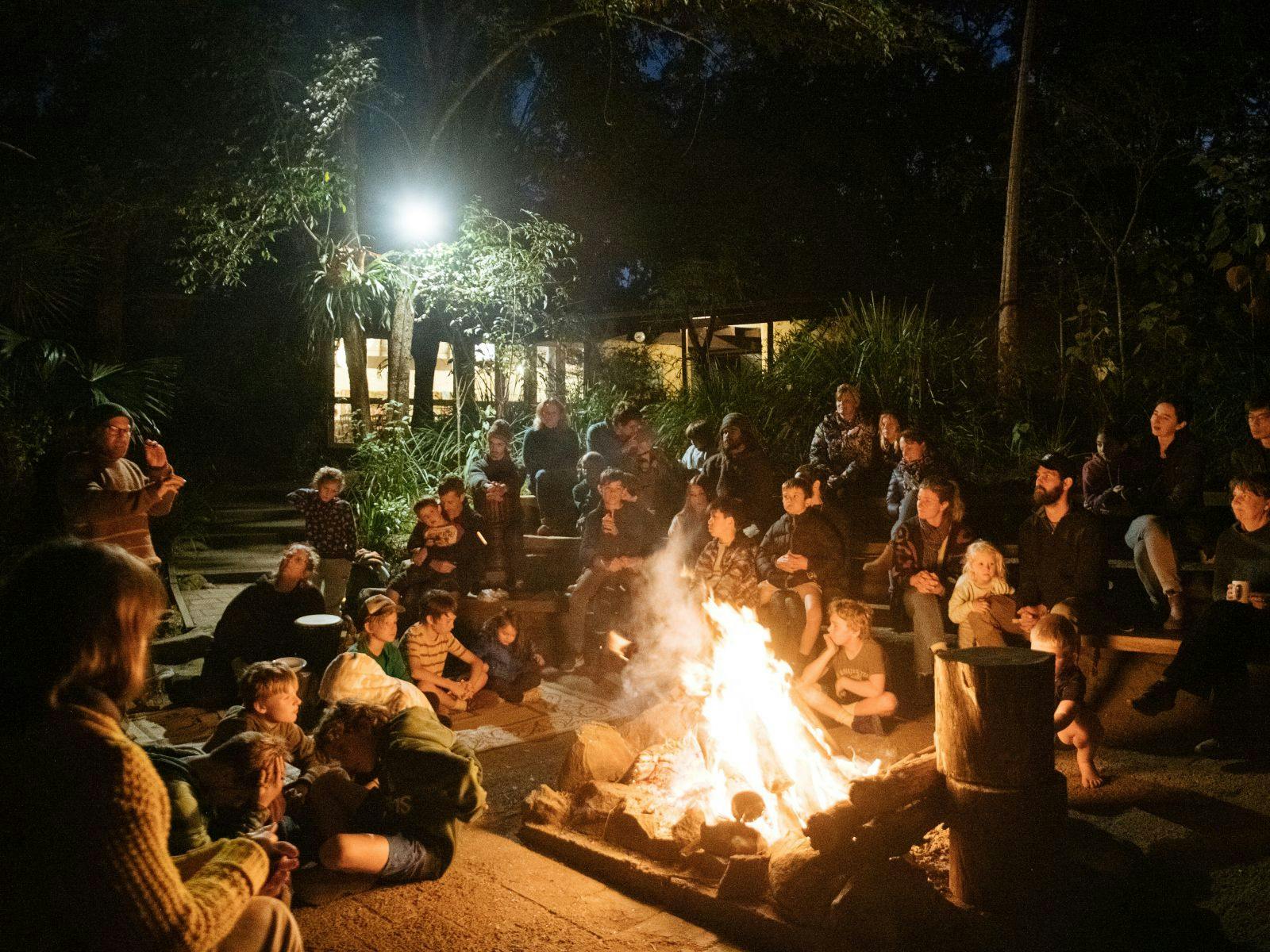 Large group of people sit around large outoor fire pit at Wangat Lodge, Hunter Valley near Dungog