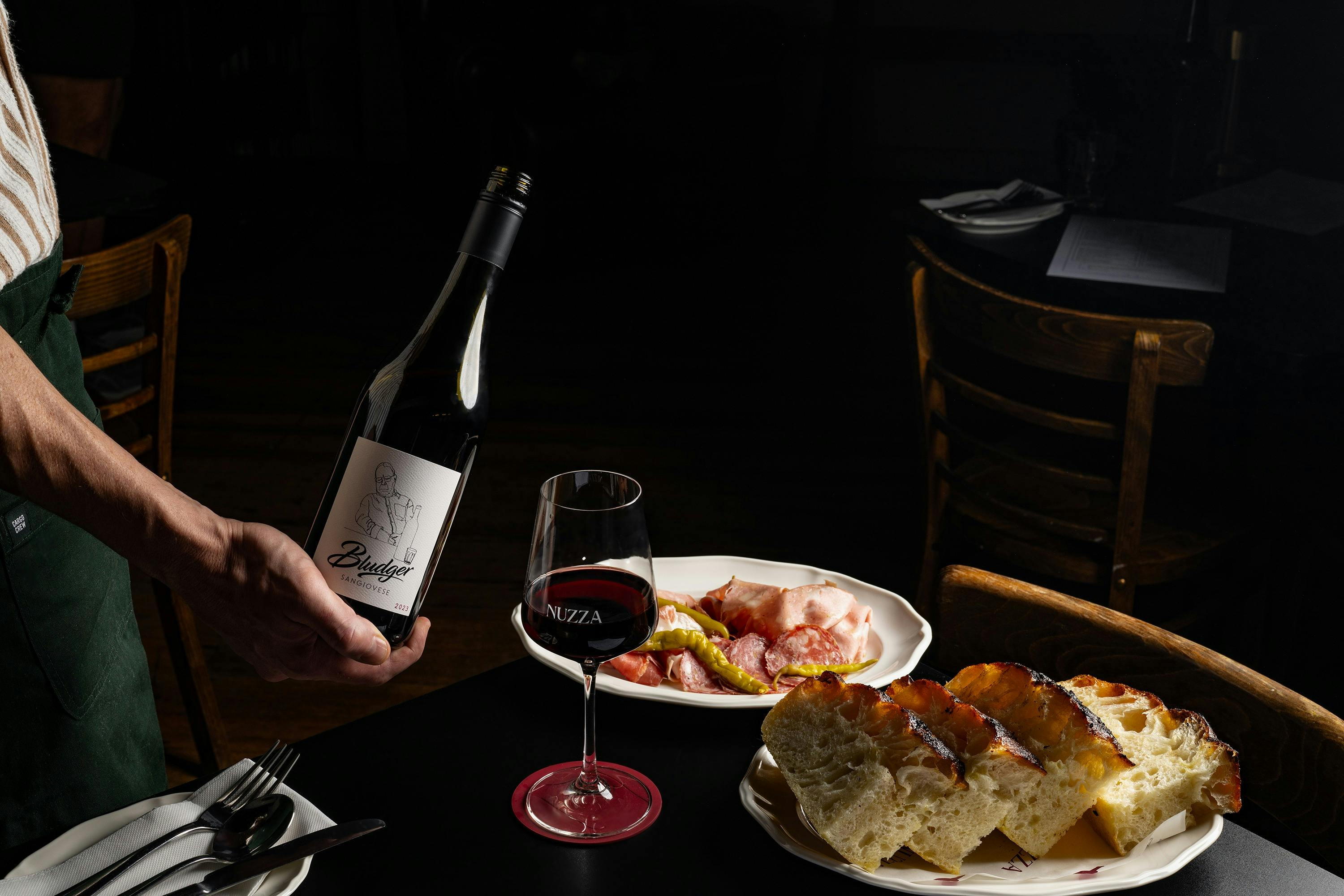 A bottle of Bludger Sangiovese, produced by Nuzza's owner, being poured into a wine glass alongside