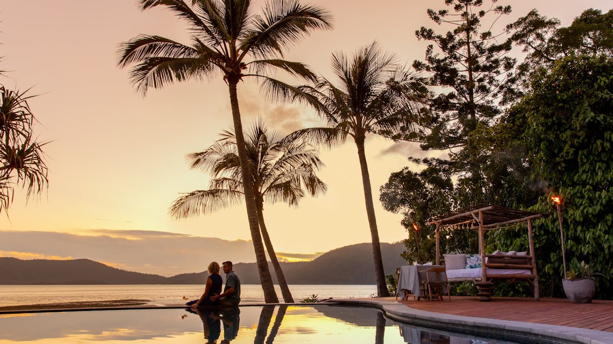 A couple enjoying a sunset at a poolside overlooking the water and mountains in the background A couple enjoying a sunset at a poolside overlooking the water and mountains in the background