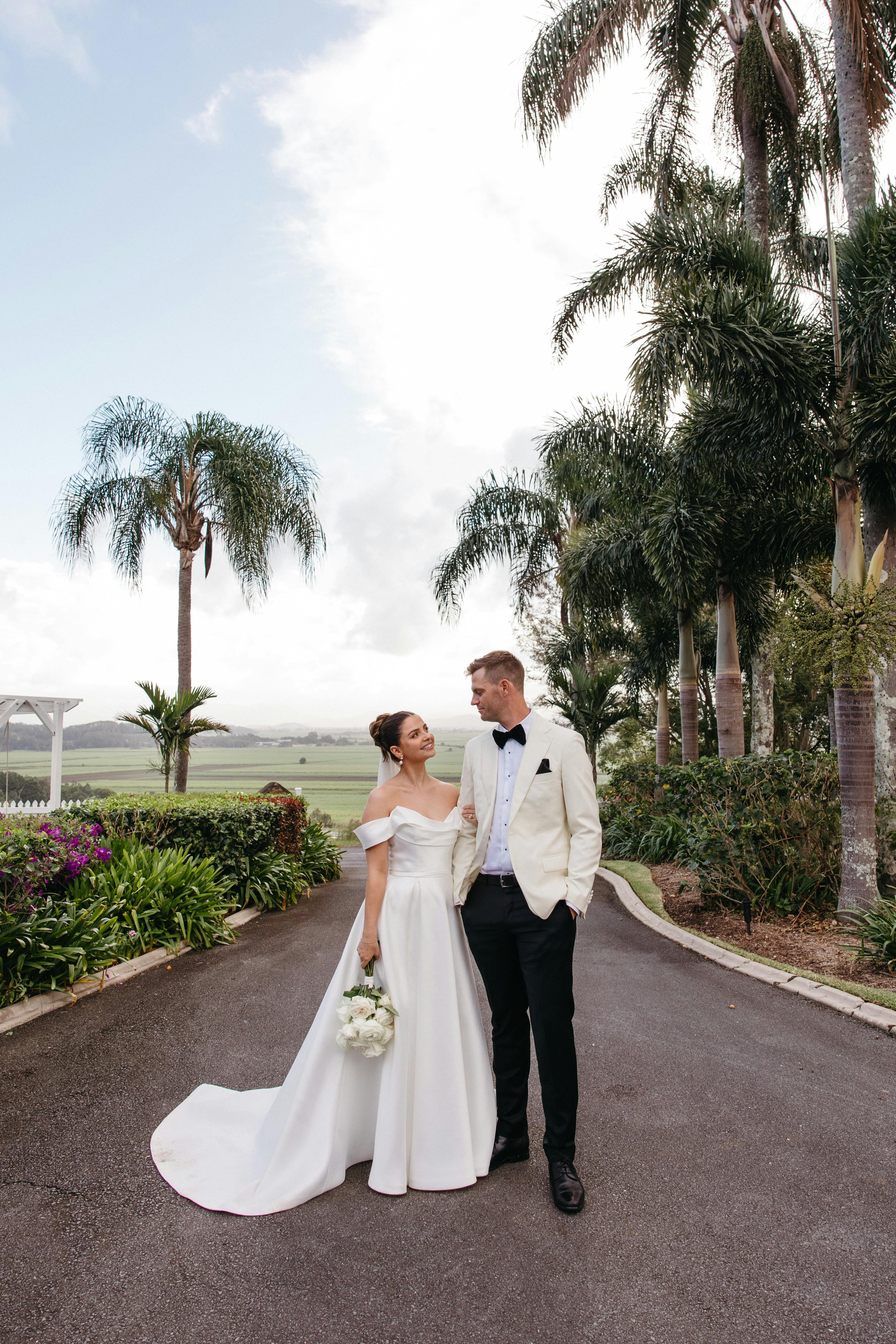 bride and groom standing in a driveway surrounded by palm trees