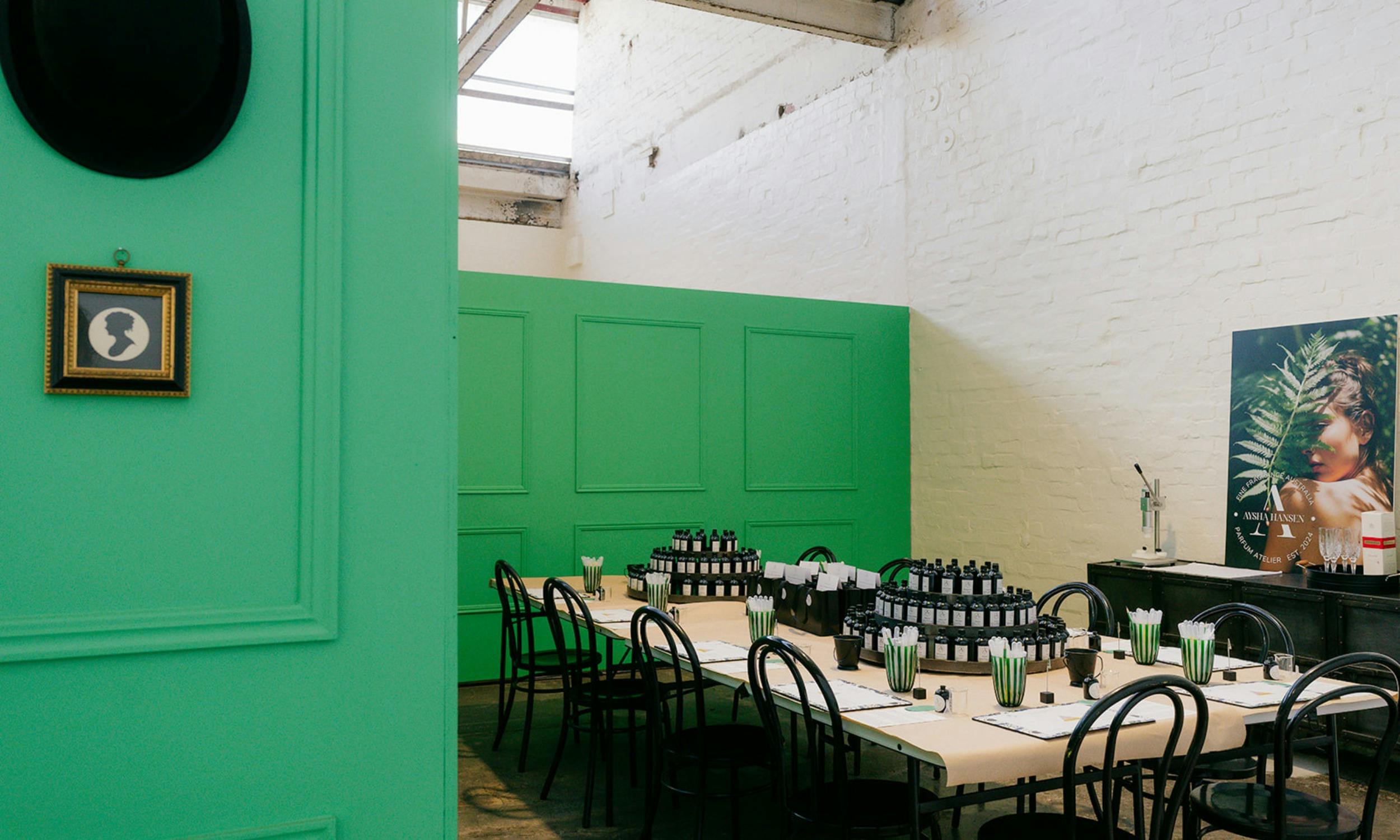 A workshop space set with perfume making tools, black bottles and green accents on long tables.