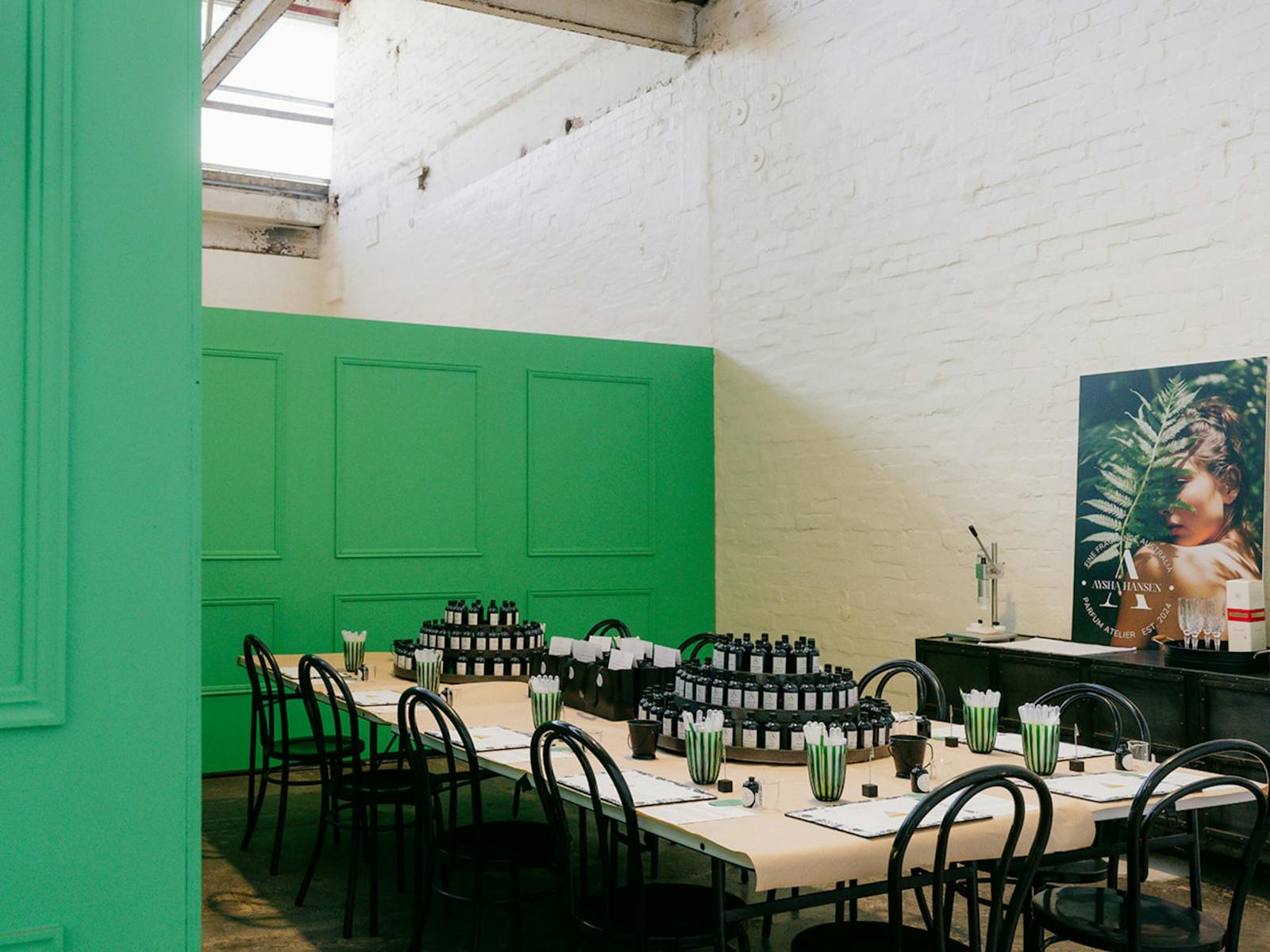 A workshop space set with perfume making tools, black bottles and green accents on long tables.