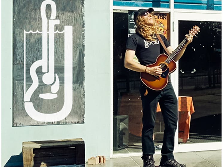 Man with long hair playing guitar on street