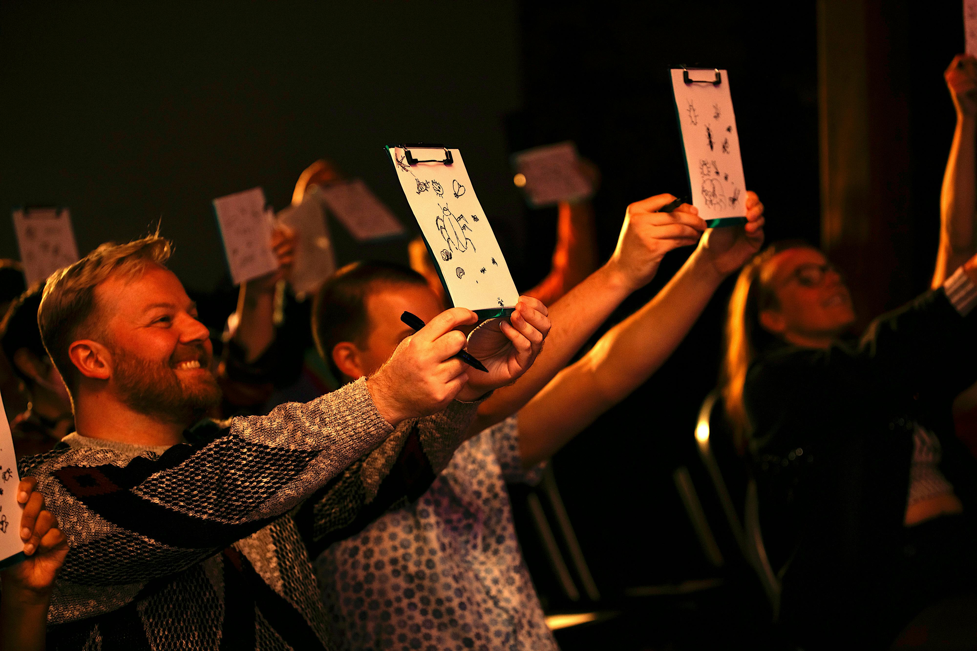 Two men are holding up clipboards with drawings of bugs