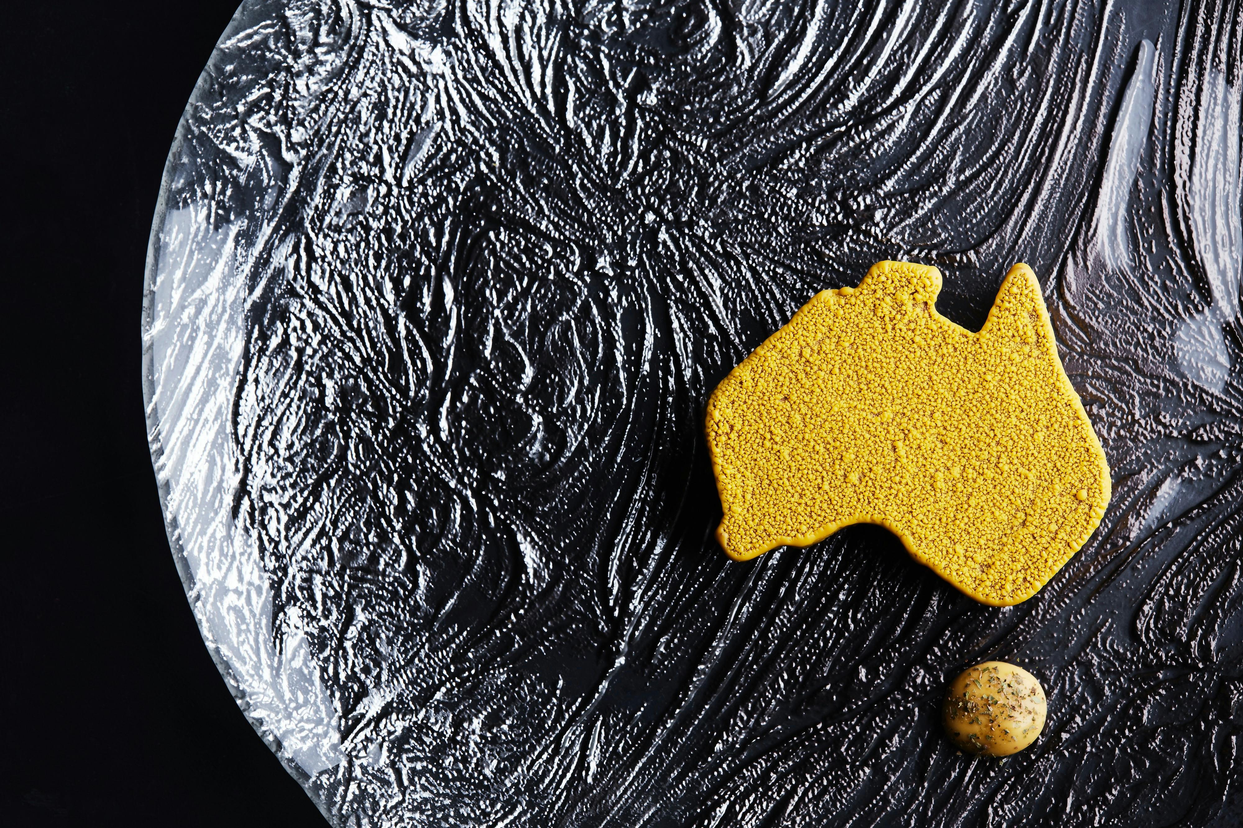 Image of a yellow dessert in the shape of Australia  sitting on a glass plate