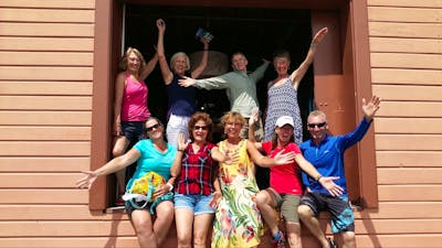Eight women and one man in large doorway smiling arms up
