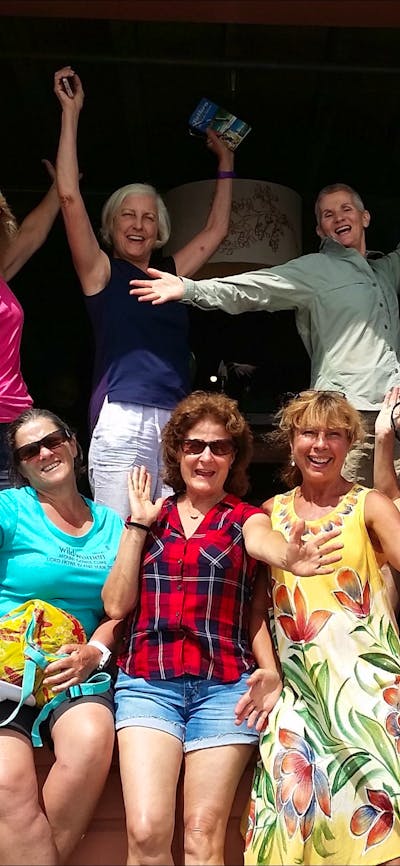 Eight women and one man in large doorway smiling arms up