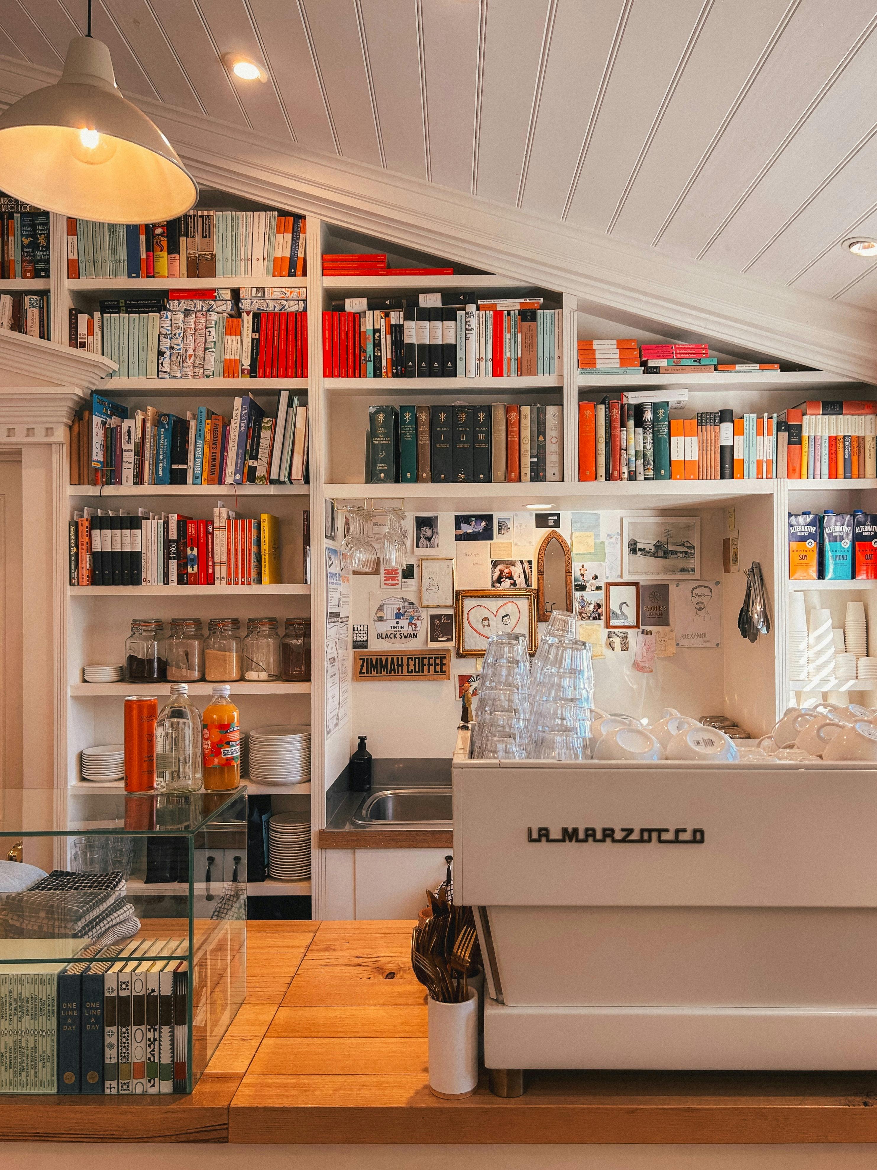 Espresso machine and cups beside shelves of books in a cosy bookshop.