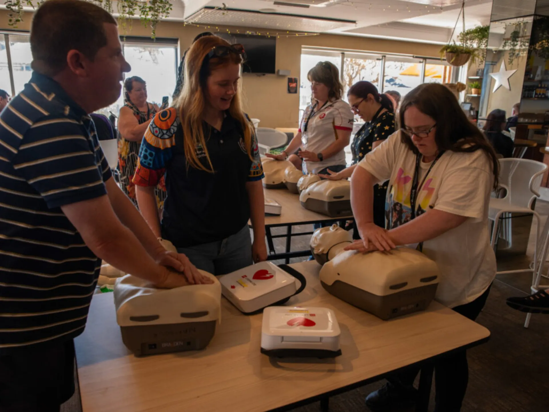 An instructor helping two people with practising CPR on a CPR doll