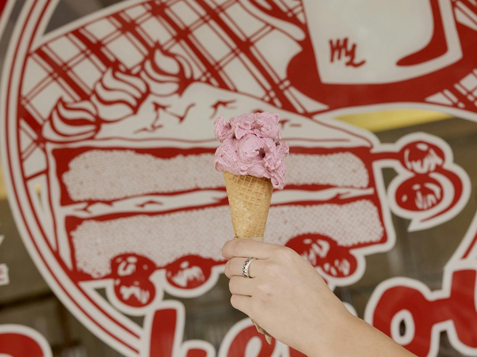 Hand holding waffle cone with strawberry gelato in front of shopfront window