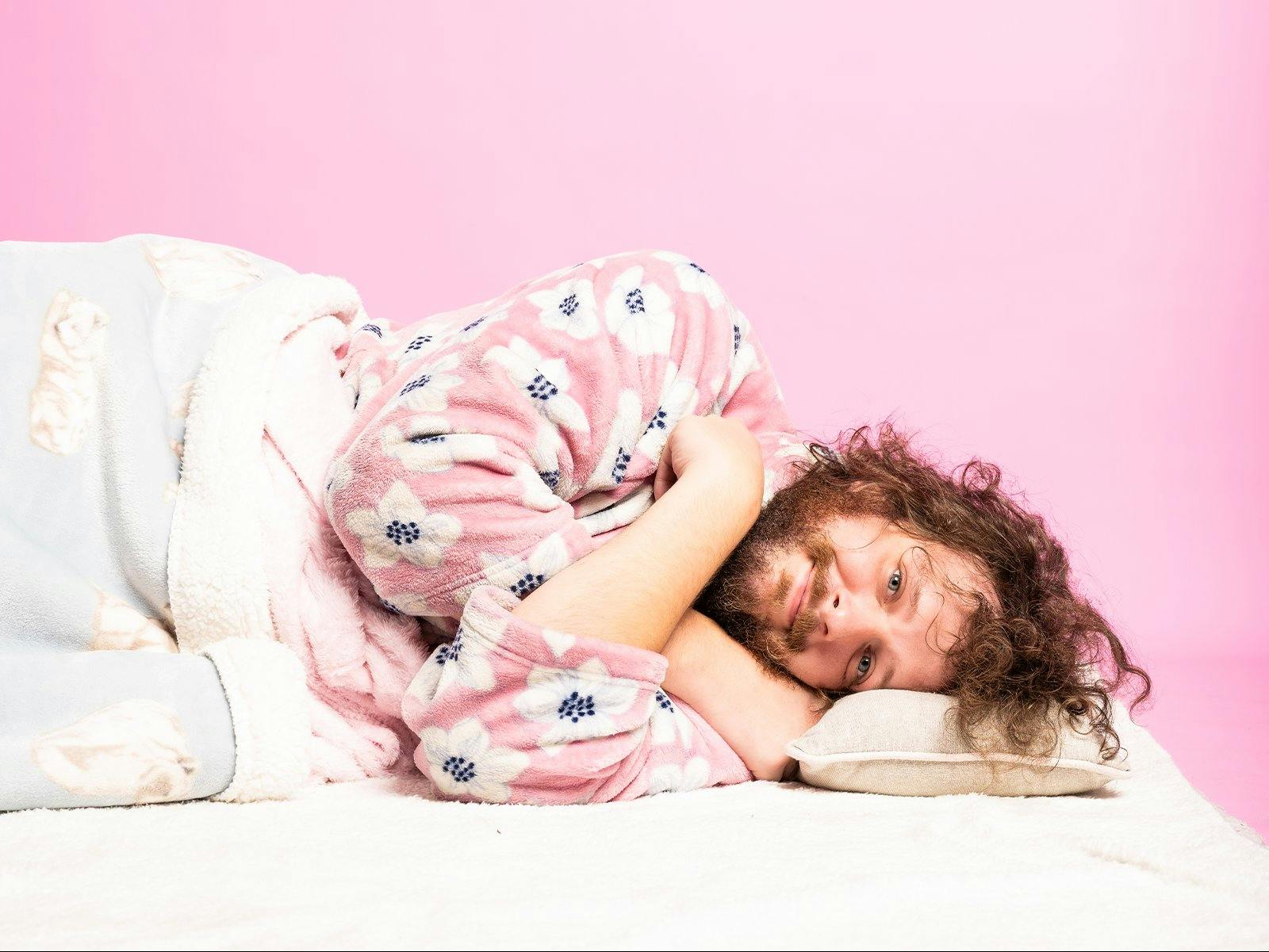 Blake lies down in a pink dressing gown with a blanket over him