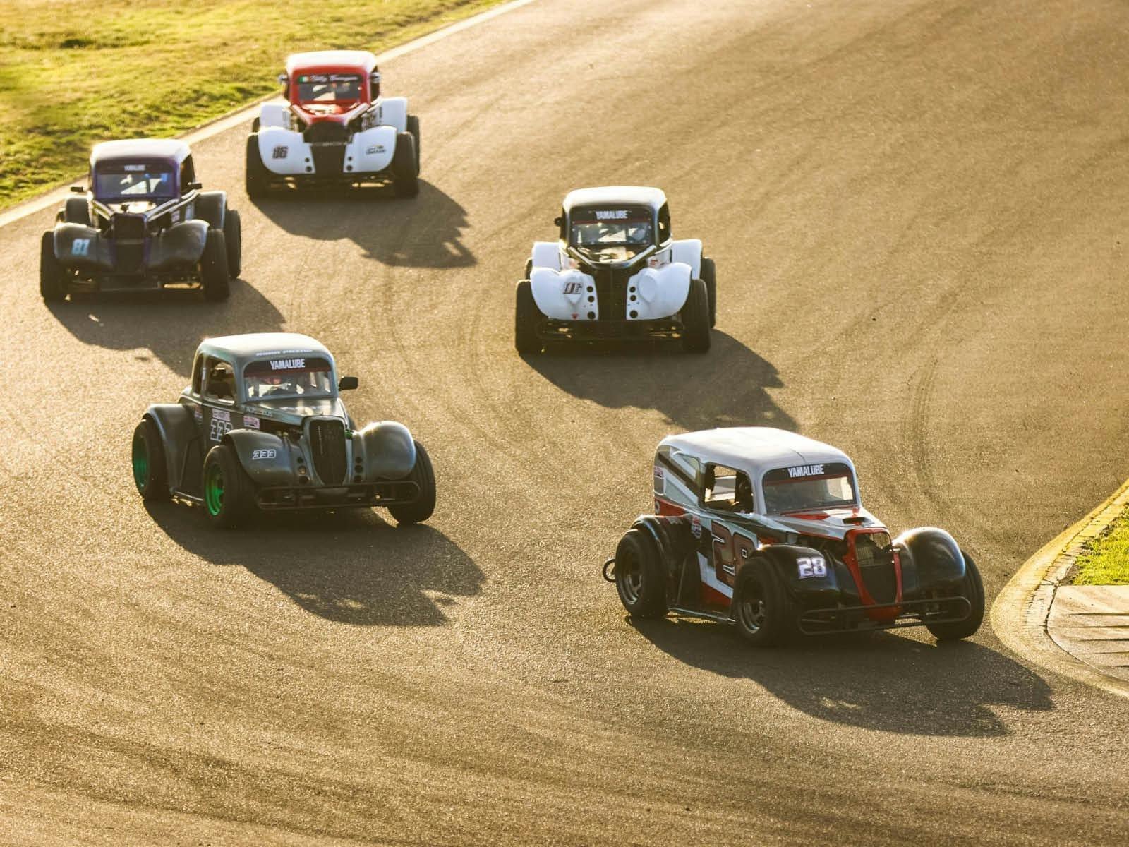 Five legend cars racing around a corner on a racetrack