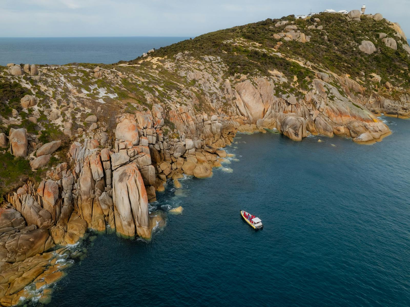 Aerial view of boat in ocean next to rocky cliffs on a peninsula with the ocean in the distance