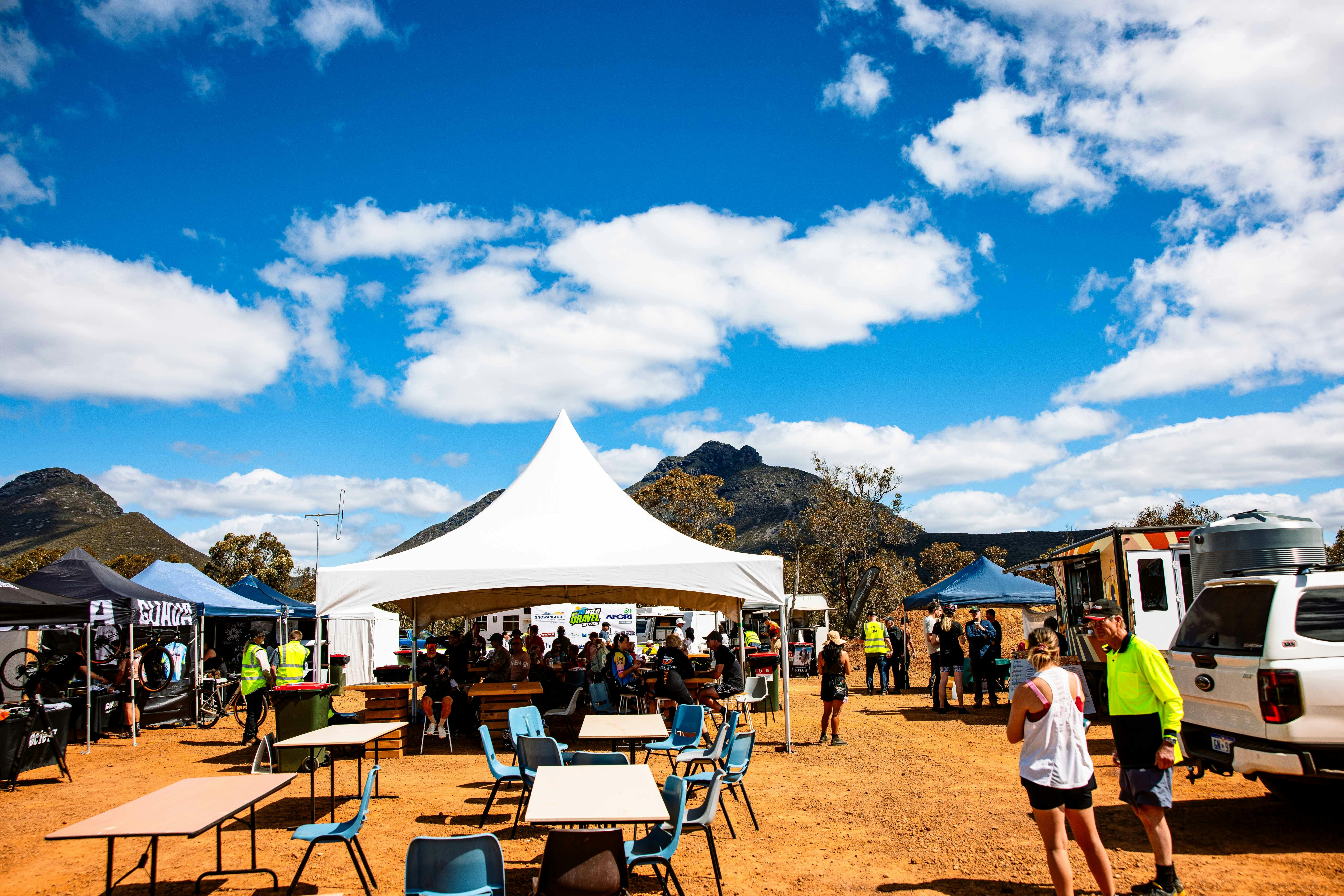 Large marquee in middle of gravel opening with tables, chairs, food vendors and people