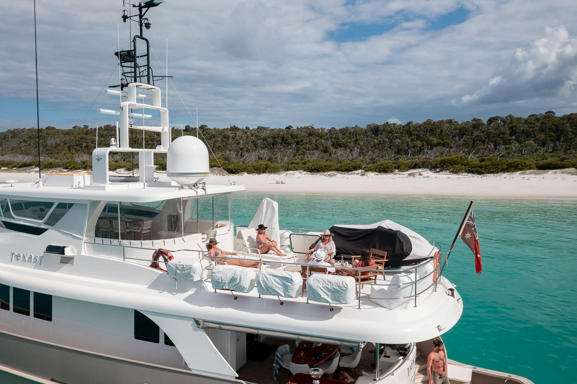 Close up drone image of guests sunbathing on sundeck of Texas T motor yacht at Whitehaven Beach