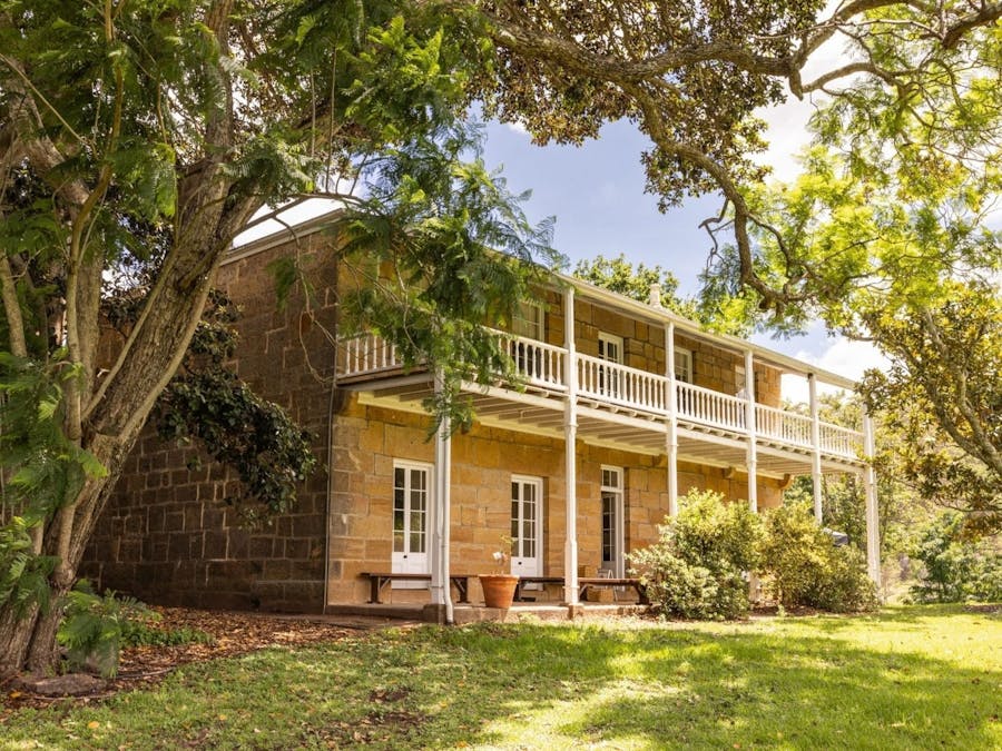 A historic sandstone two storey Homestead photographed from the exterior with fig tree in foreground