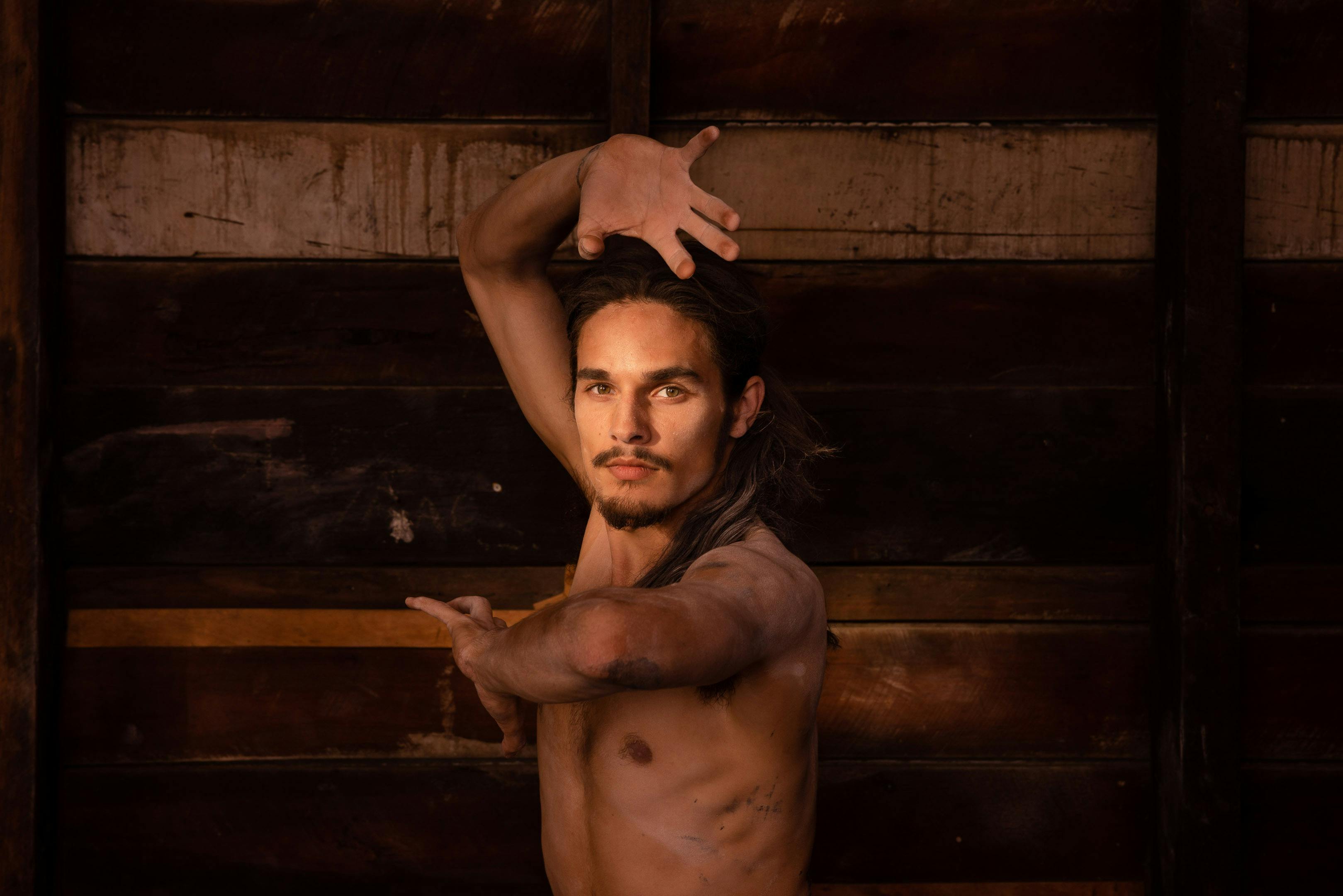 A dancer poses in front of an exposed wooden warehouse wall