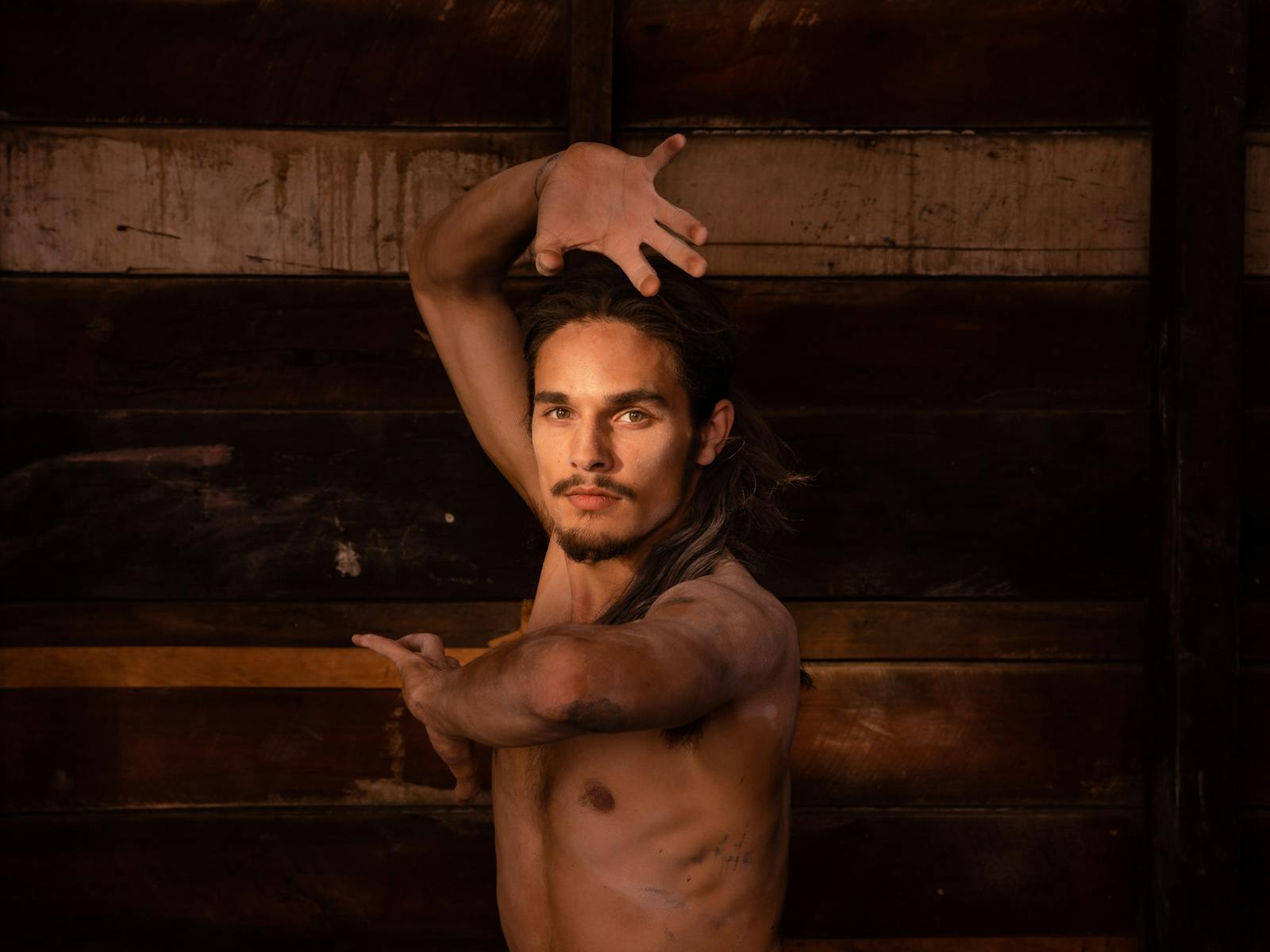 A dancer poses in front of an exposed wooden warehouse wall