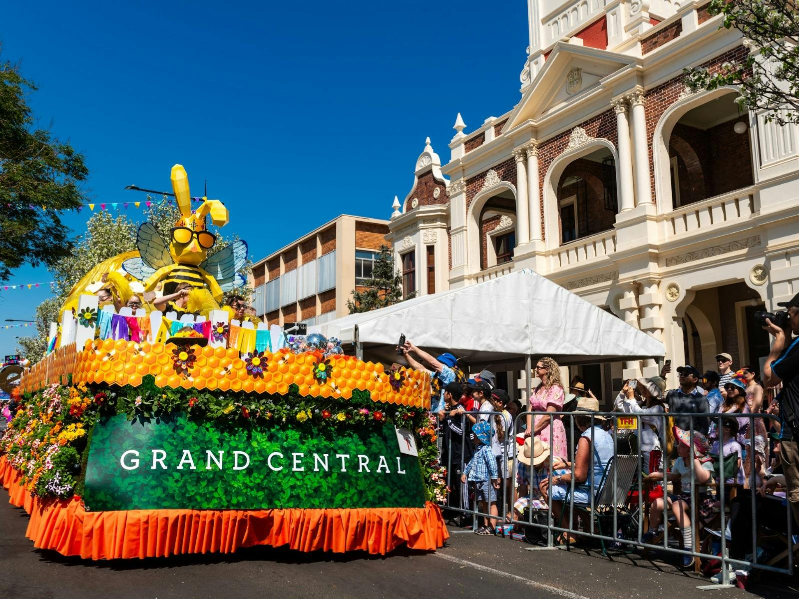 The grand central floral parade float with flowers and bee all decorated on it. People cheering The grand central floral parade float with flowers and bee all decorated on it. People cheering