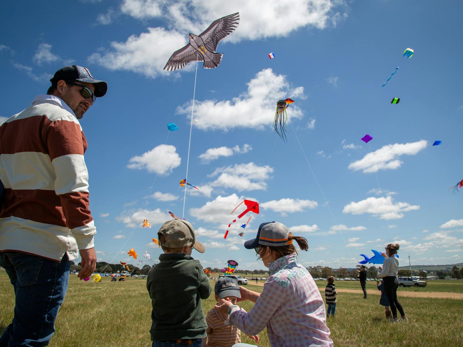 Parents teaching son how to fly a kite amongst other kite flyers.