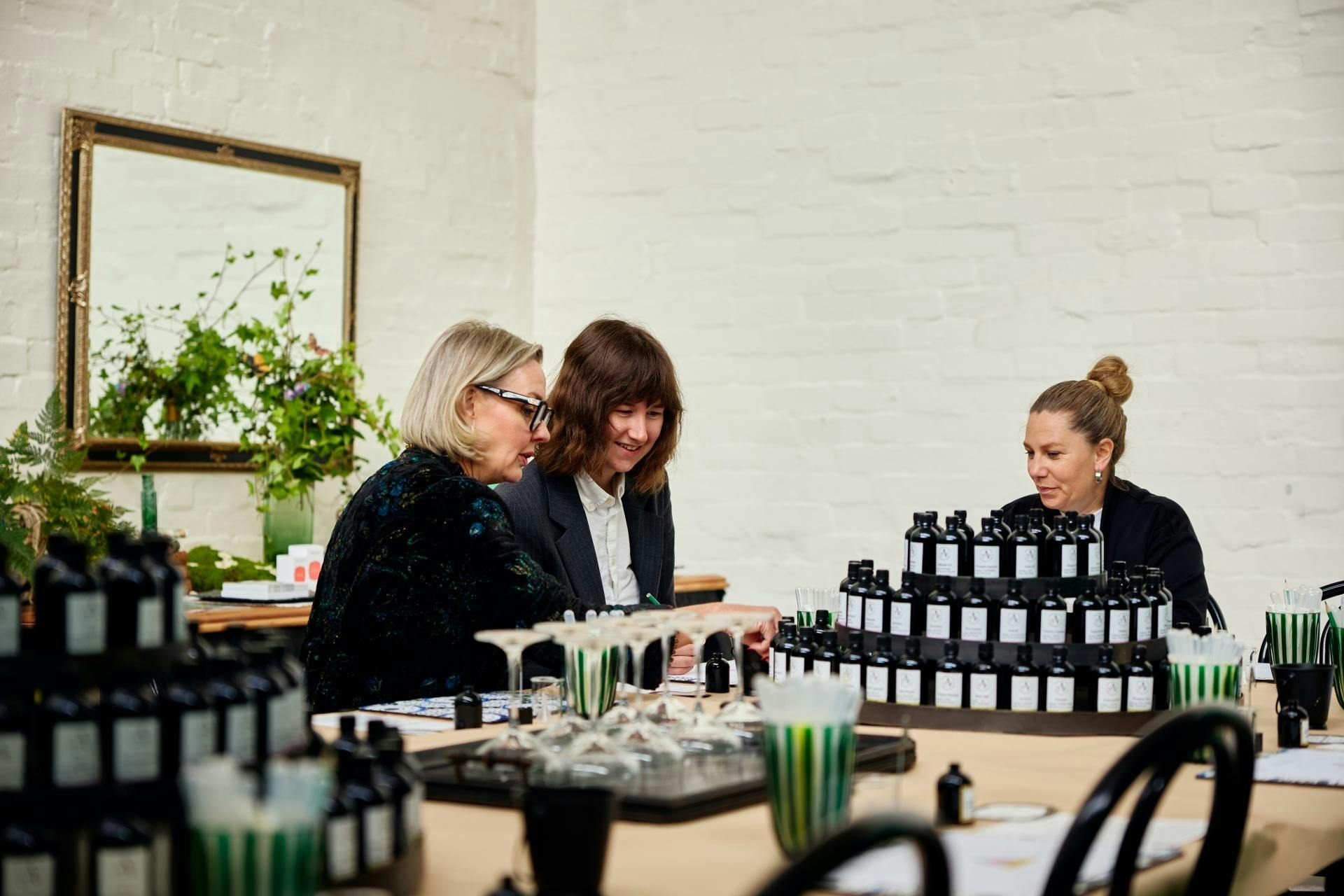 three women looking at stacks of fragrance bottles