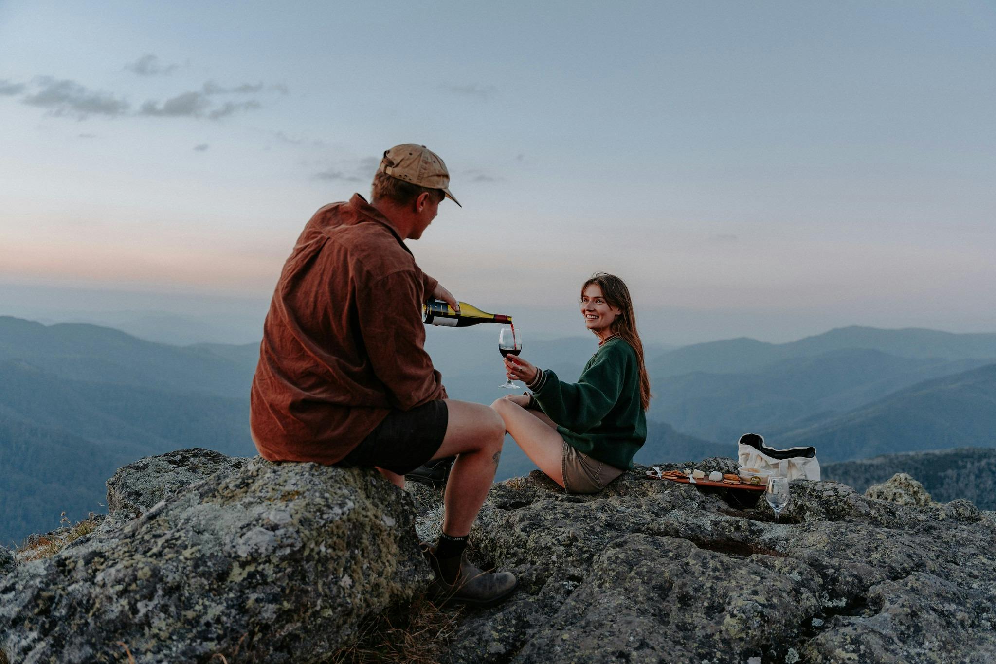 A couple pours wine for each other during a picnic at blue hour on the top of Mt Mckay.