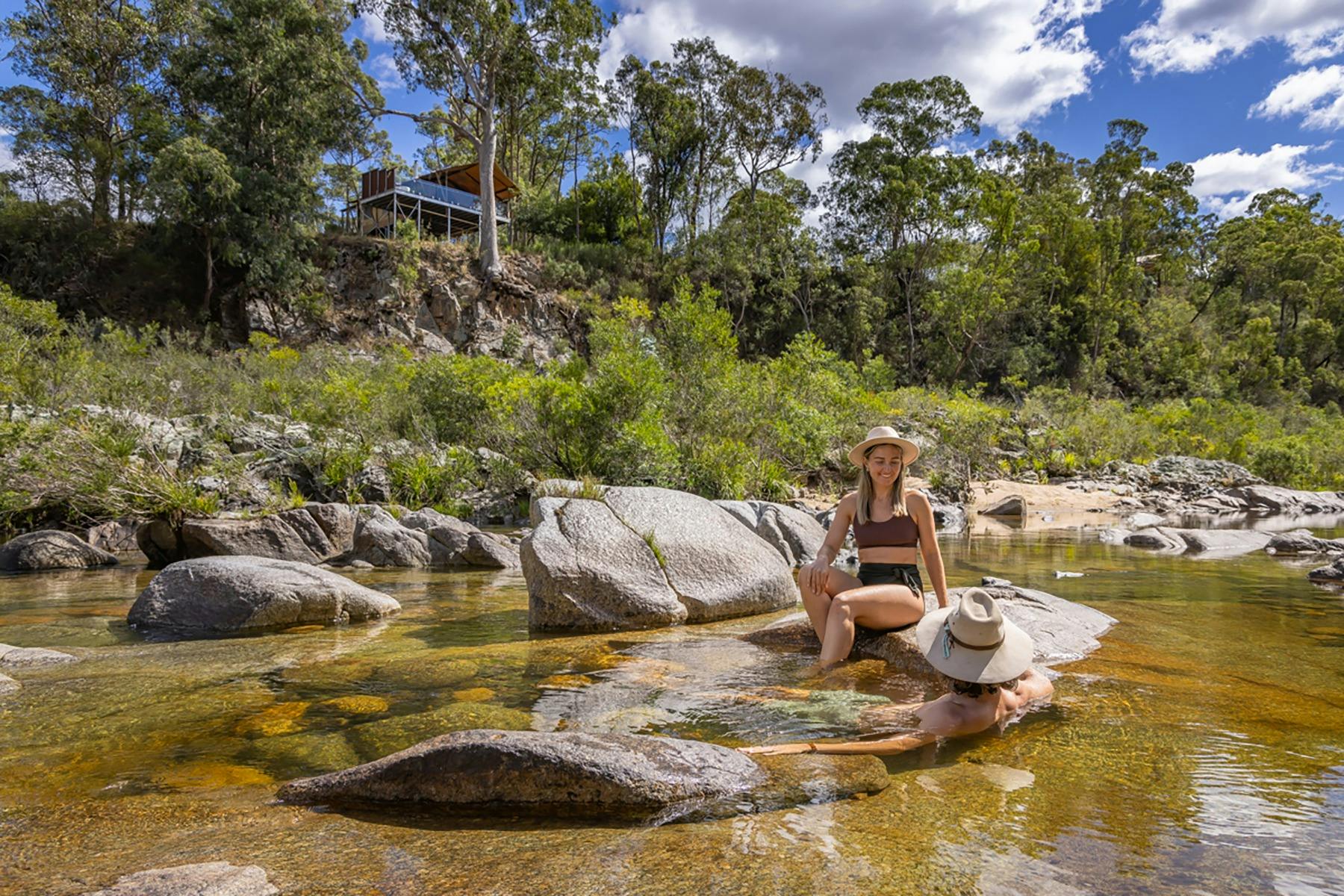 崖の上のテントを背景に、川の遊泳用の穴に座っているカップル