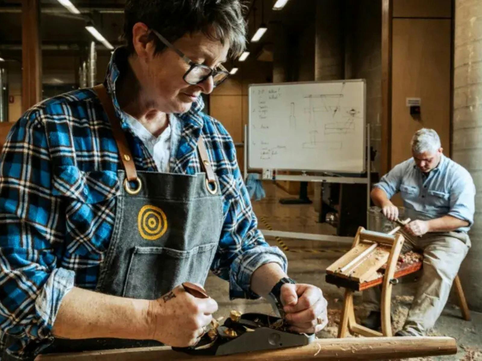 Two men seated and carving wood inside workshop
