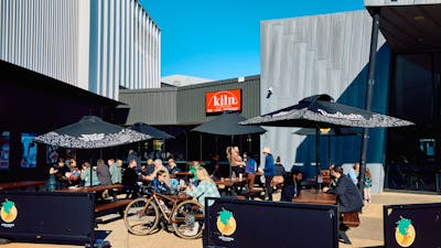 The outdoor terrace of Kiln café at Belco Arts. People eat and drink beneath parasols on a sunny day