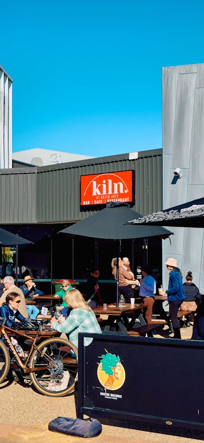 The outdoor terrace of Kiln café at Belco Arts. People eat and drink beneath parasols on a sunny day