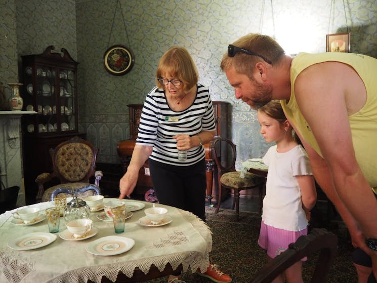 A man and child admire a fine tea party set up on display by a female guide
