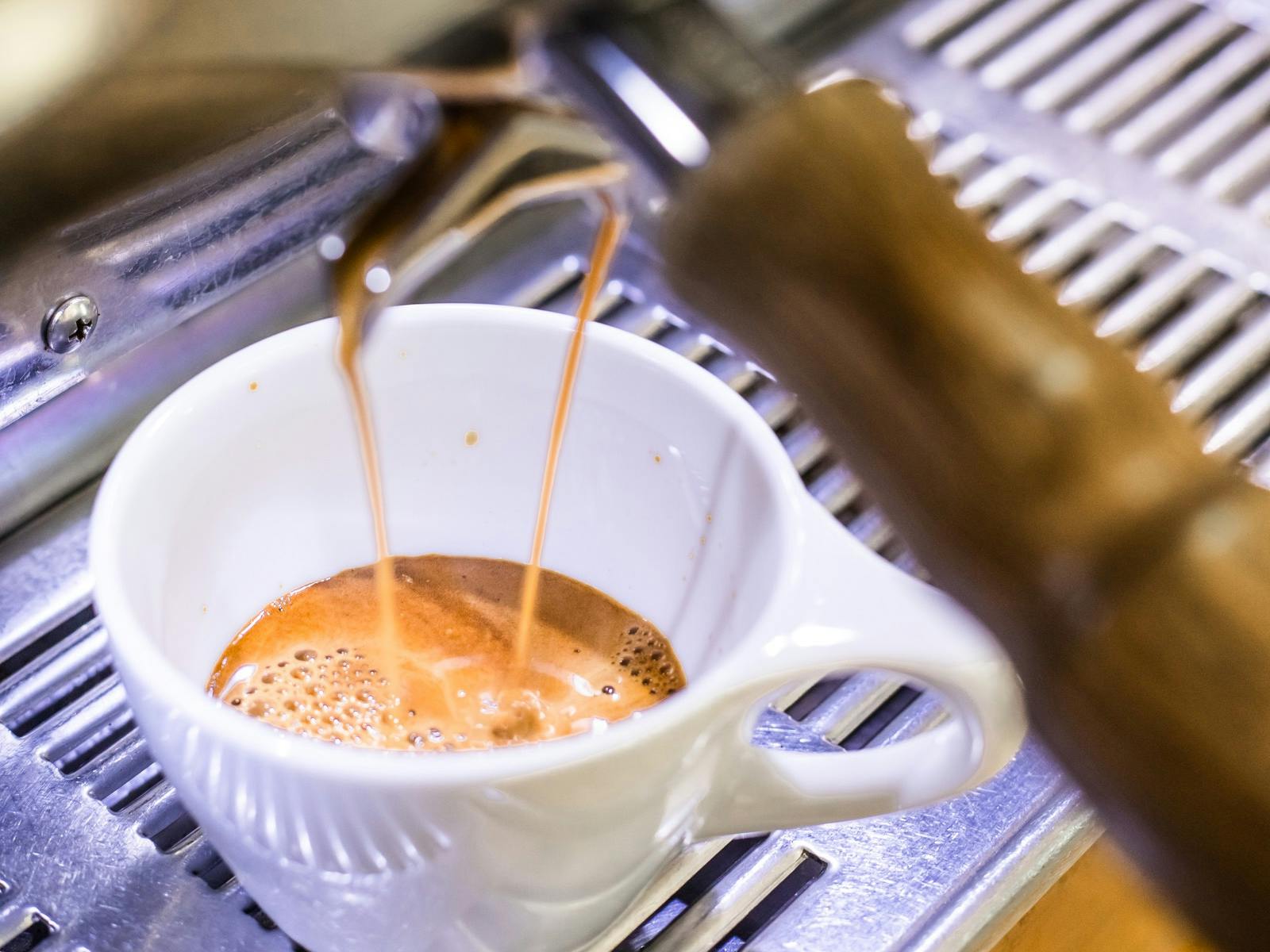 A close up of a double espresso shot pouring out of the machine into a white cup