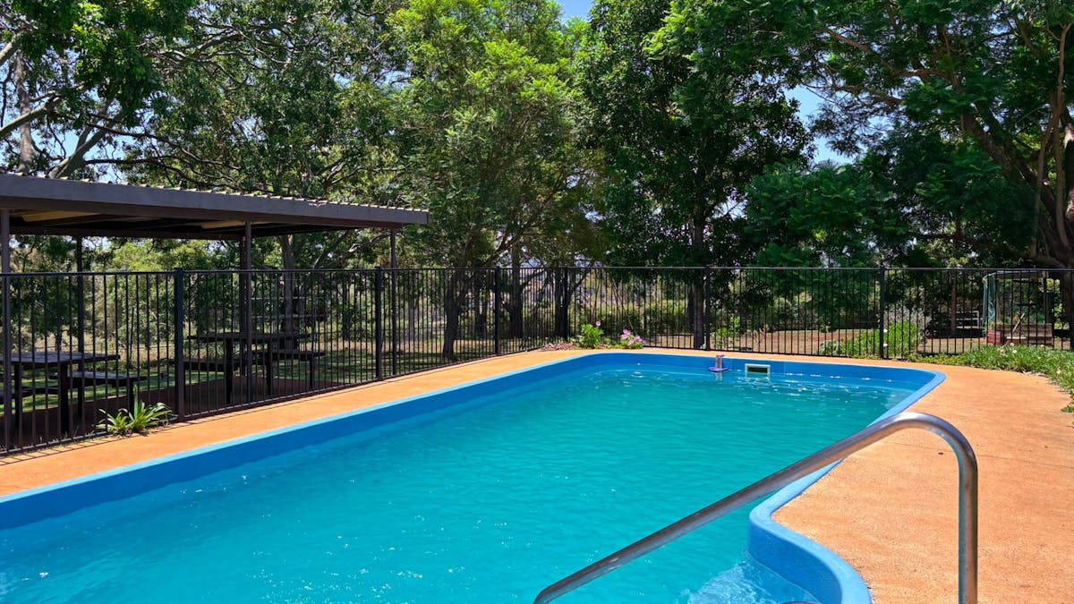 Outdoor swimming pool with surrounding fencing and shaded seating area at Yarraman Caravan Park