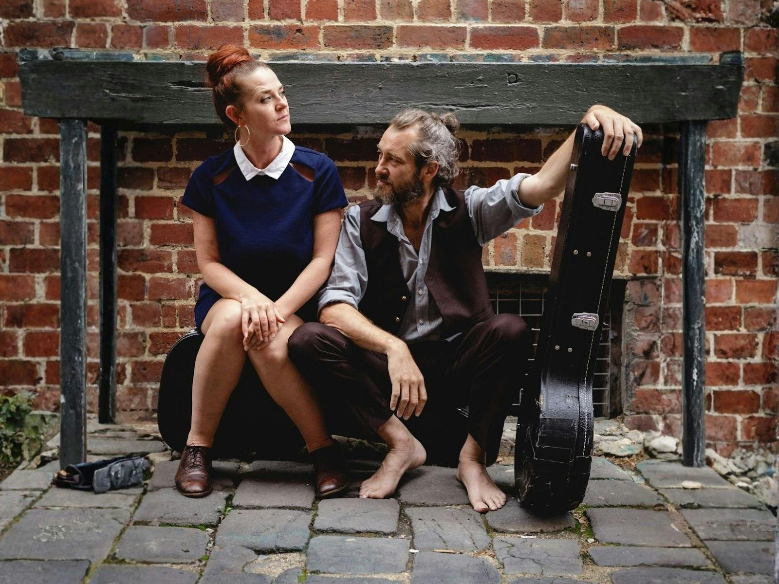 A Male and female sit in front of a brick wall, staring in opposite directions.