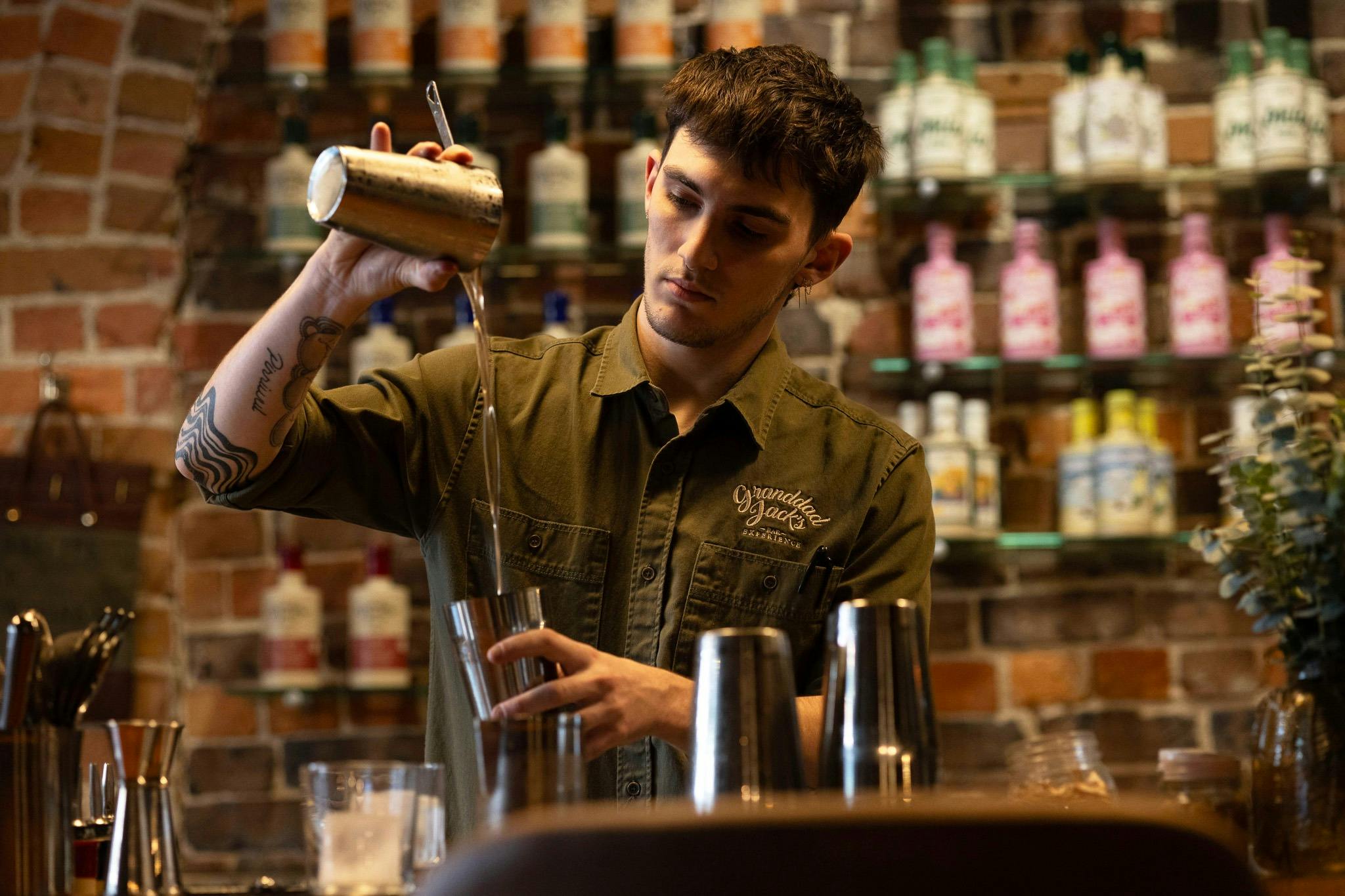 Hunter, a staff member at Granddad's Bar pouring a cocktail into a cocktail shaker.