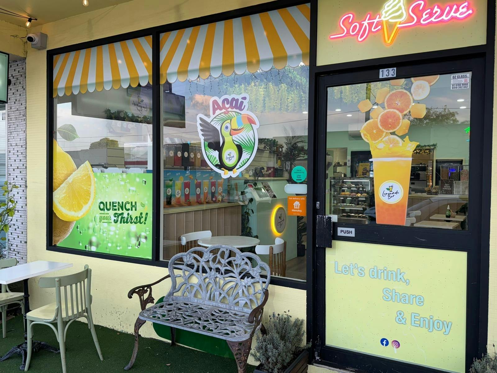 Storefront of Lemonade Bar featuring colorful drink graphics, soft serve ice cream sign, glass entry