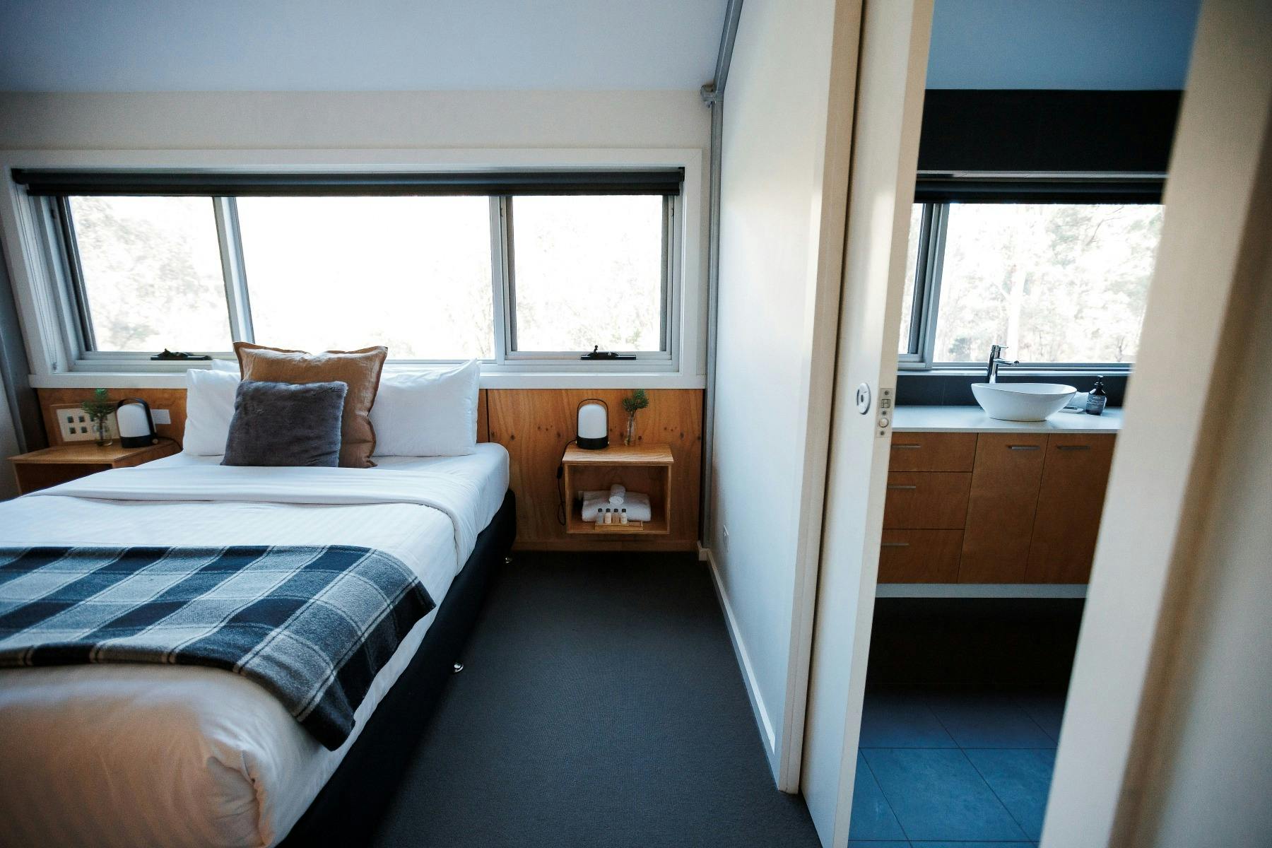 Warm toned queen bedroom, window over bed with views of bushland and sliding door to  bathroom