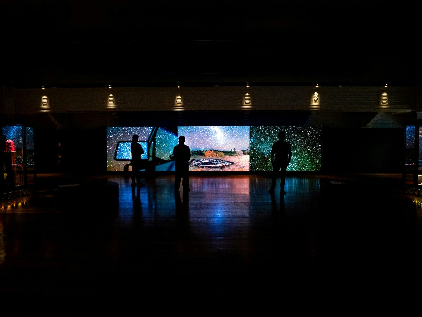 Dark gallery space with shadows and outlines of people in the space