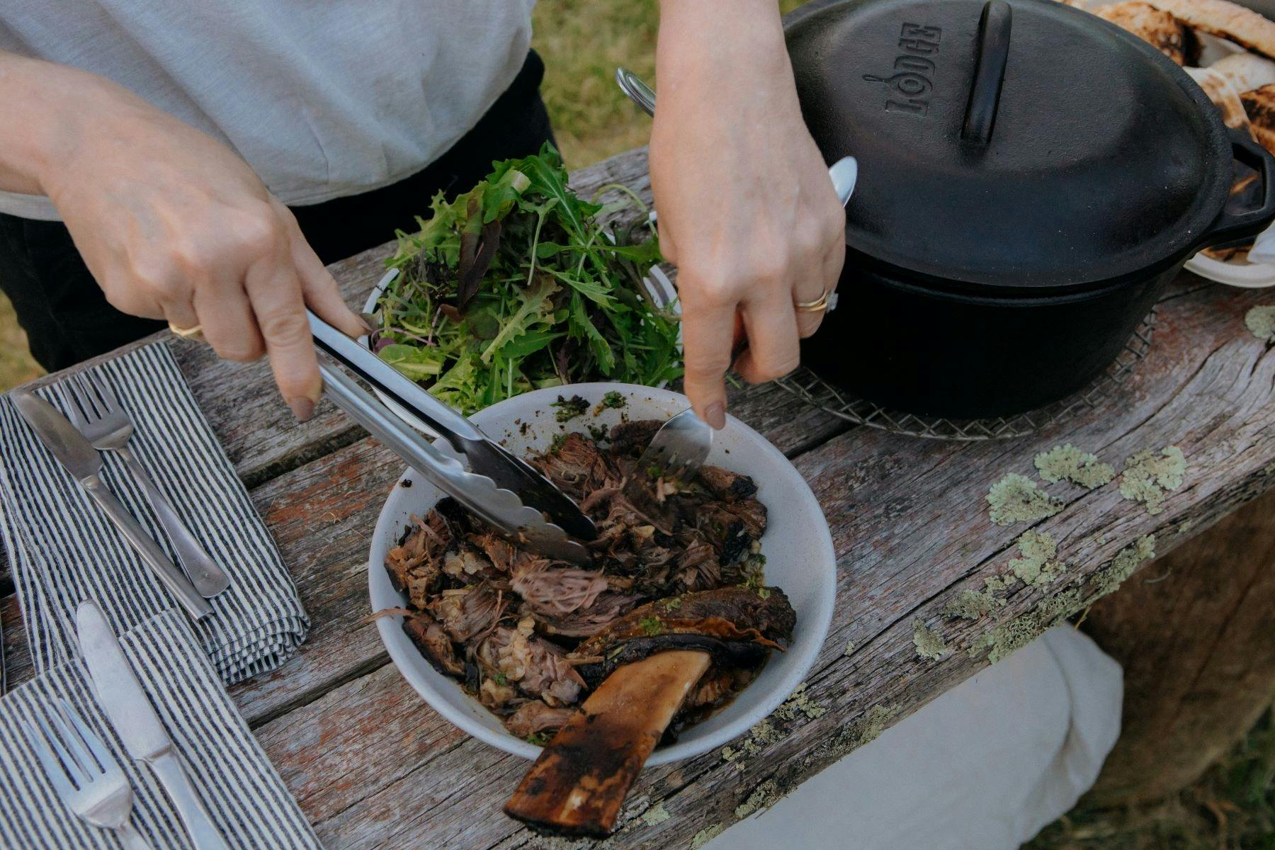 Woman pulling slow braised beef from rib in bowl with salad greens accompanying