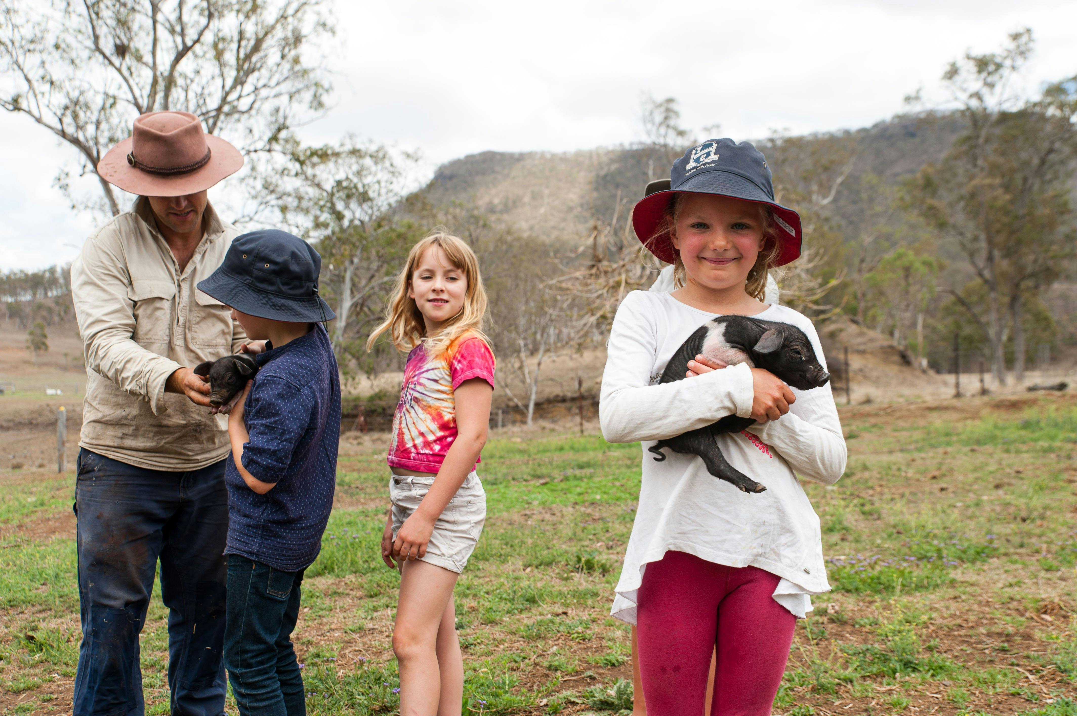 Child holing piglet with farmer