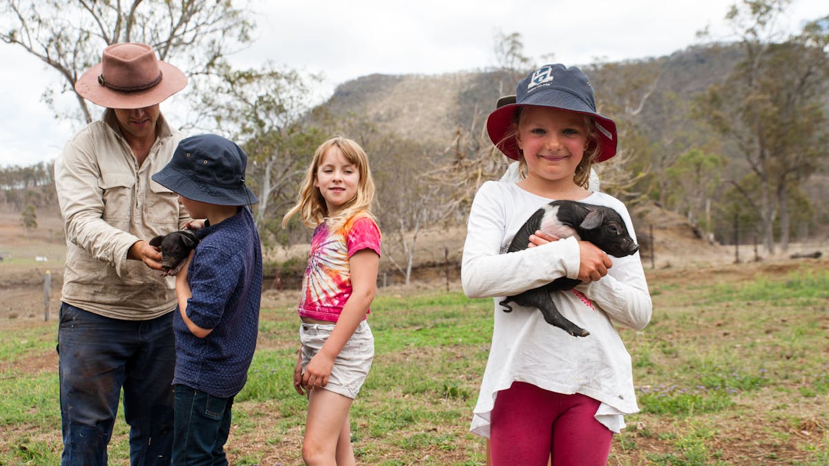 Child holing piglet with farmer