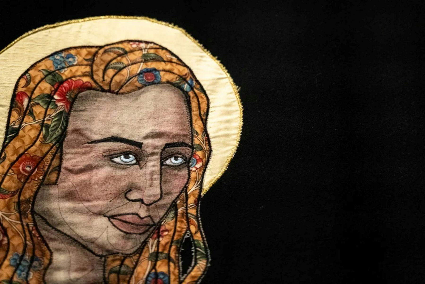 A close up of a quiltyed textile artwork showing a womans face with a yellow halo behind her head