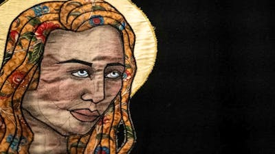 A close up of a quiltyed textile artwork showing a womans face with a yellow halo behind her head