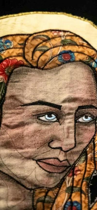 A close up of a quiltyed textile artwork showing a womans face with a yellow halo behind her head